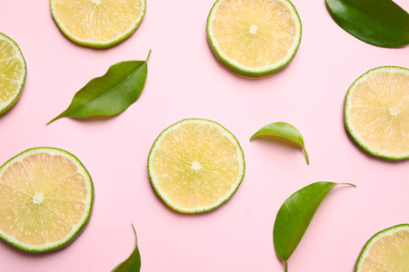 Juicy fresh lime slices and green leaves on pink background, flat lay