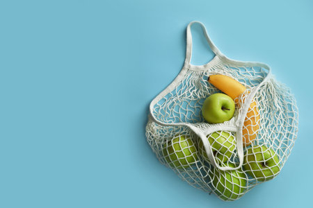 Net bag with fruits on light blue background, top view. Space for textの写真素材