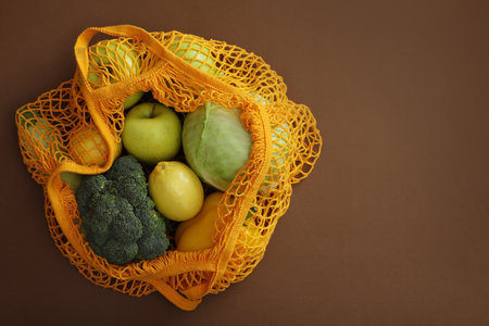 Net bag with fruits and vegetables on brown background, top view. Space for textの写真素材