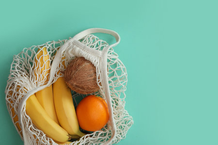Net bag with fruits on turquoise background, top view. Space for textの写真素材