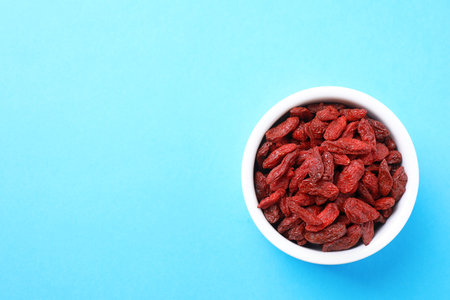Dried goji berries in bowl on light blue background, top view. Space for textの写真素材