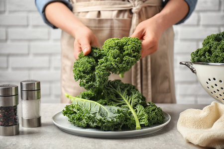 Woman holding fresh kale leaves over light gray table, closeupの写真素材
