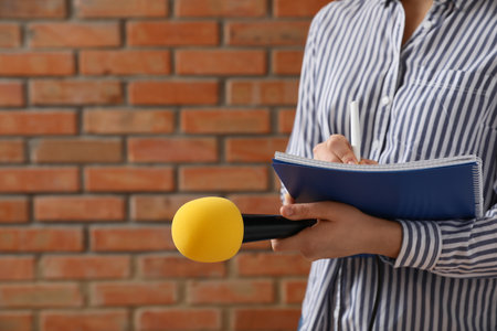 Journalist with microphone and notebook near brick wall, closeupの写真素材