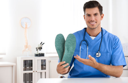 Handsome male orthopedist showing insoles in clinicの写真素材
