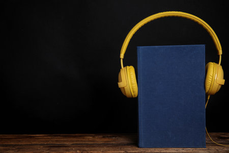 Book and modern headphones on wooden table against black background. Space for textの写真素材