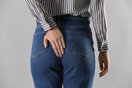 Woman suffering from hemorrhoid on light gray background, closeup