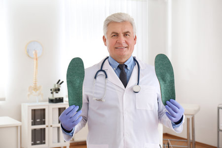 Senior male orthopedist showing insoles in clinicの写真素材