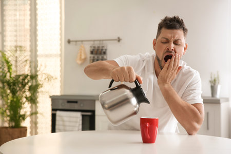 Sleepy man pouring coffee into cup at home in the morningの写真素材