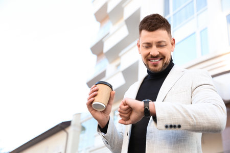 Businessman with cup of coffee on city street in the morning