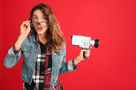Beautiful young woman with vintage video camera on red backgroundの写真素材