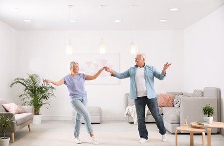 Happy mature couple dancing together in living roomの写真素材