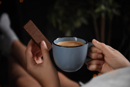Woman with wafer and coffee on dark background, closeup. early breakfastの写真素材