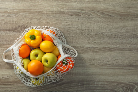 Net bag with vegetables and fruits on wooden table, top view. Space for textの写真素材