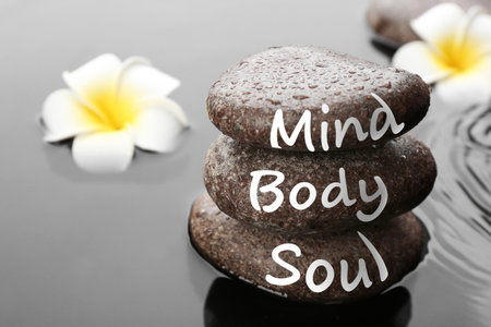 Spa stones with words Mind, Body, Soul and plumeria flowers in water, closeup. Zen lifestyleの写真素材