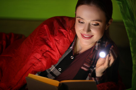 Young woman with flashlight reading book in tentの写真素材
