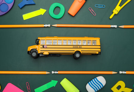 Flat lay composition with yellow school bus and stationery on green background. Transport for...