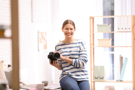 Young journalist with camera at workplace in light officeの写真素材