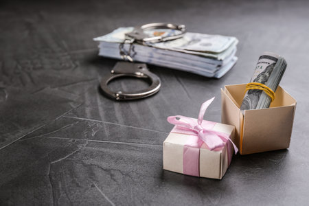 Dollar bills, gift box and handcuffs on gray stone table, space for text. Bribe concept