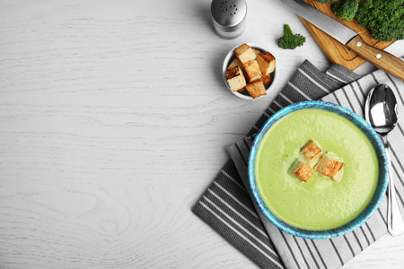 Delicious broccoli cream soup with croutons served on wooden table, flat lay. Space for textの写真素材