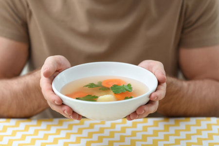 Young man holding bowl of tasty soup at table, closeupの写真素材