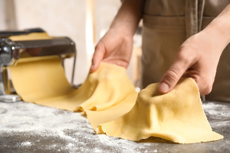 Woman preparing dough with pasta maker machine at gray table, closeupの写真素材