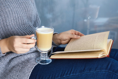 Woman with cup of coffee reading book at home, closeupの写真素材