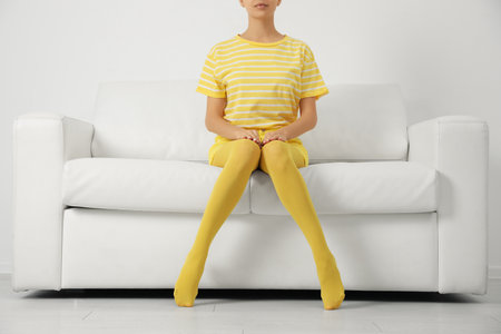 Woman wearing yellow tights sitting on sofa indoors, closeupの写真素材