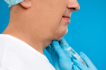Mature man with double chin receiving injection on blue background, closeup