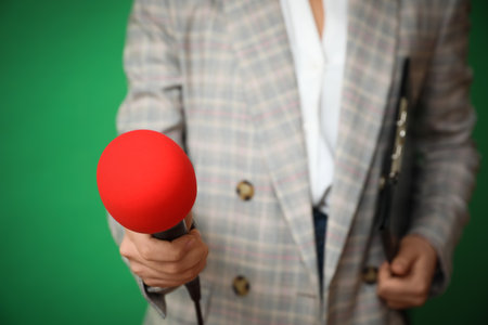 Journalist with microphone and clipboard on green background, closeupの写真素材