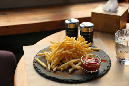 Tasty French fries with red sauce served on table in cafe