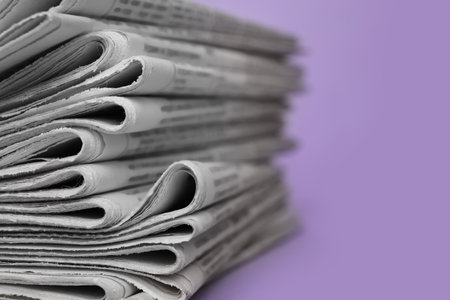 Stack of newspapers on light violet background, closeup. Journalist's work
