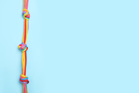 Top view of colorful ropes tied together on light blue background, space for text. unity concept