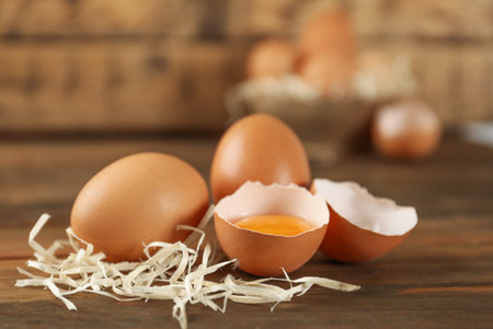 Raw brown chicken eggs and decorative straw on wooden table
