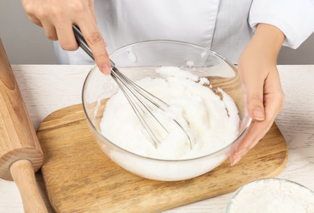 Woman whipping egg whites at wooden table, closeup. Baking-pie