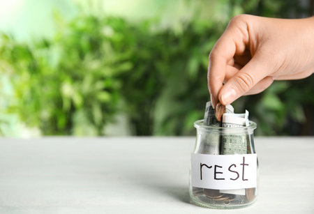 Woman coin into jar with tag REST on white wooden table, closeup. Space for textの写真素材