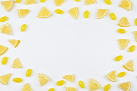 Frame made with fresh lemon slices and tasty candies on white table, flat lay. Space for textの写真素材