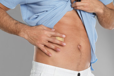 Man with sticking plaster on tummy against light gray background, closeup