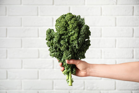 Woman holding fresh kale leaves near white brick wall, closeupの写真素材