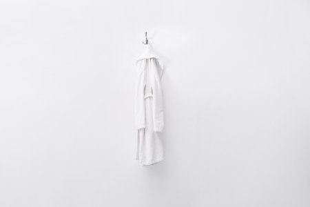 Fresh white bathrobe hanging on light wallの写真素材