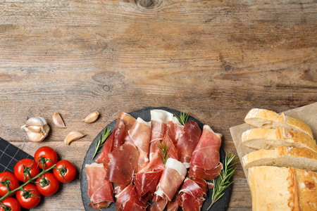 Pile of tasty prosciutto on wooden table, flat lay. Space for textの写真素材