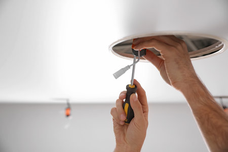 Worker installing lamp on stretch ceiling indoors, closeupの写真素材