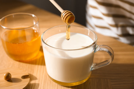 Adding honey to milk on wooden table, closeupの写真素材