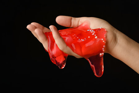 Woman playing with red slime on black background, closeup. antistress toyの写真素材