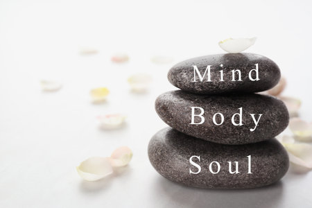 Stones with words MIND, BODY, SOUL and petals on light background, space for text. Zen lifestyleの写真素材
