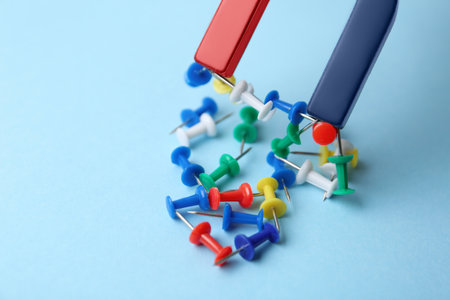 Magnet attracting colorful pins on light blue background, closeupの写真素材