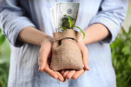 Woman holding sack with dollars and green sprout, closeup. money savingsの写真素材