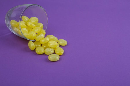 Delicious lemon drops and glass on purple background. Space for textの写真素材