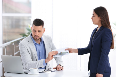 Woman giving bribe to man at table indoorsの写真素材