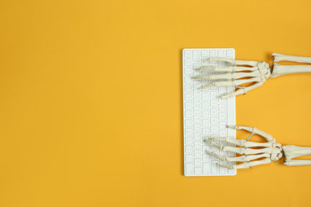 Human skeleton using computer keyboard on yellow background, top view. Space for textの写真素材
