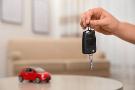 Man holding key near table with miniature automobile model indoors, closeup. car buyingの写真素材